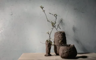 Wabi-sabi stílusú kézzel készült kerámia vázák virágzó ágakkal mészfesték textúrájú fal előtt